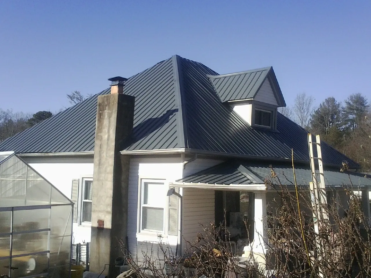 Dark blue standing seam metal roof on a white farmhouse with dormer — Slate & Tile Roof Repair by Roofing Brothers in Wellford