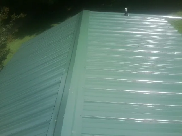 New green metal panels meeting at the ridge of a roof — Flat Roof Repair work by our crew in Wellford