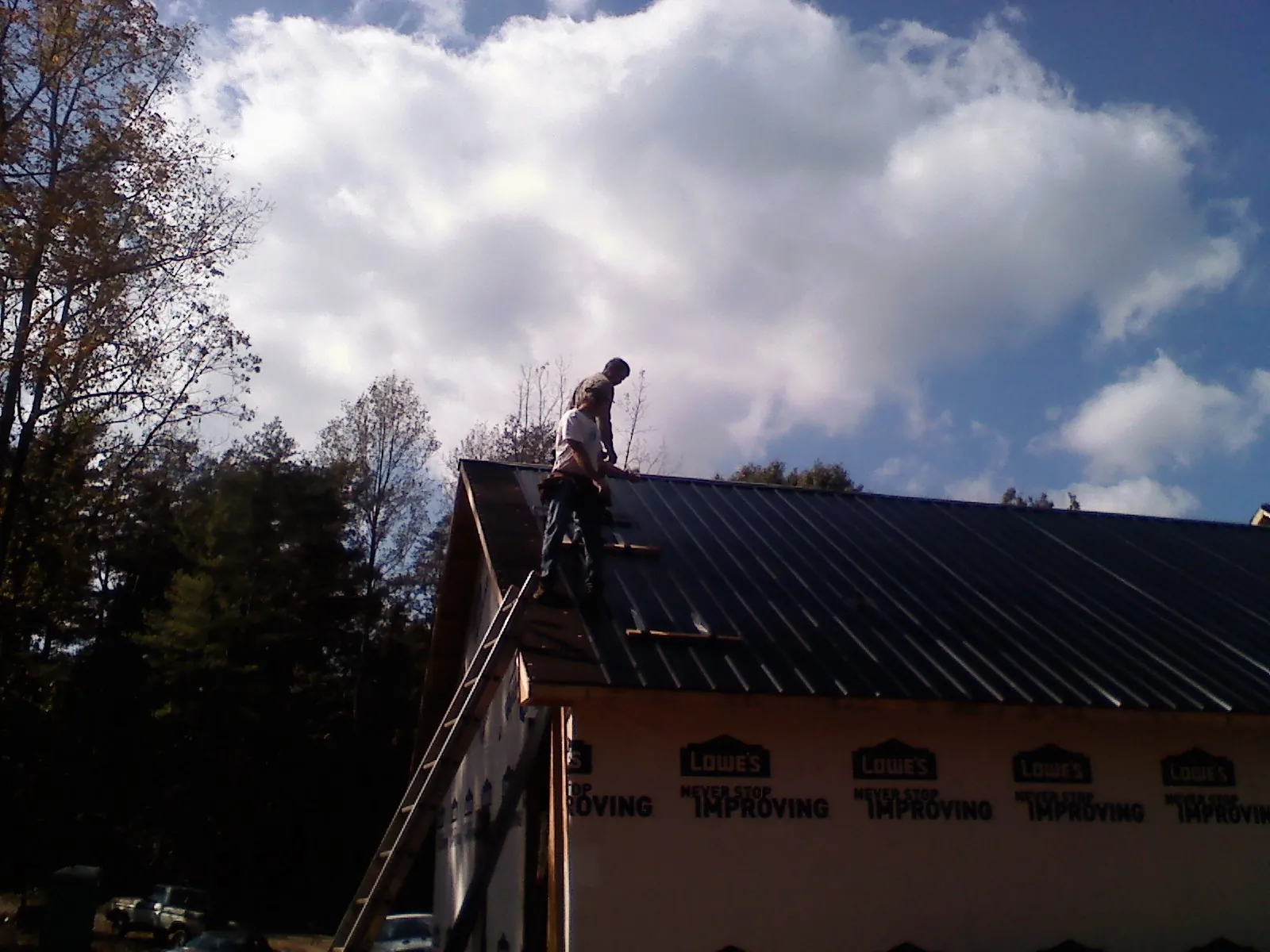Roofer fastening dark metal panels high against a cloudy sky, from a Roof Inspection job in Wellford