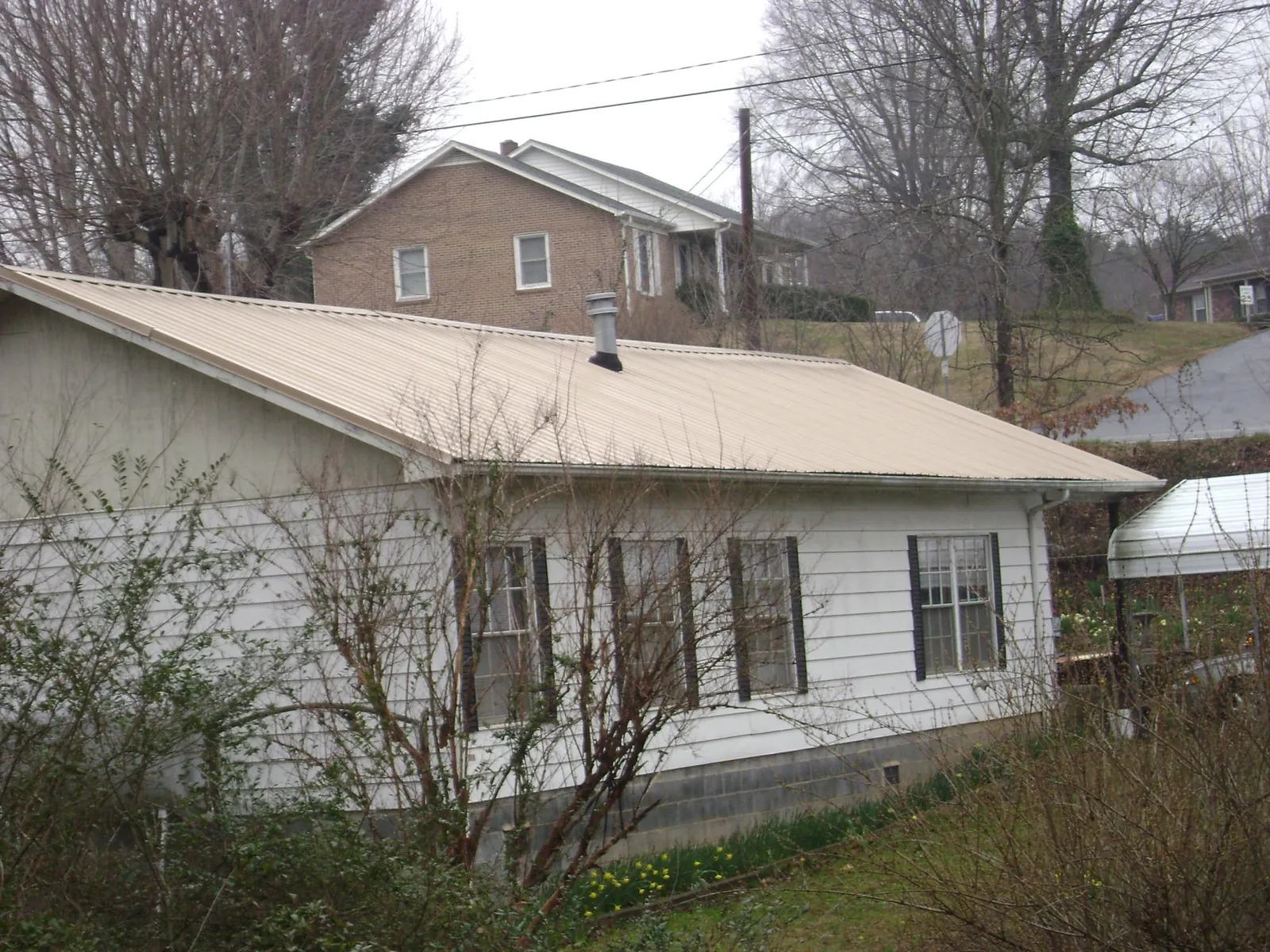 Tan metal roof on a white sided house set into a hillside — Commercial Roofing by Roofing Brothers in Wellford